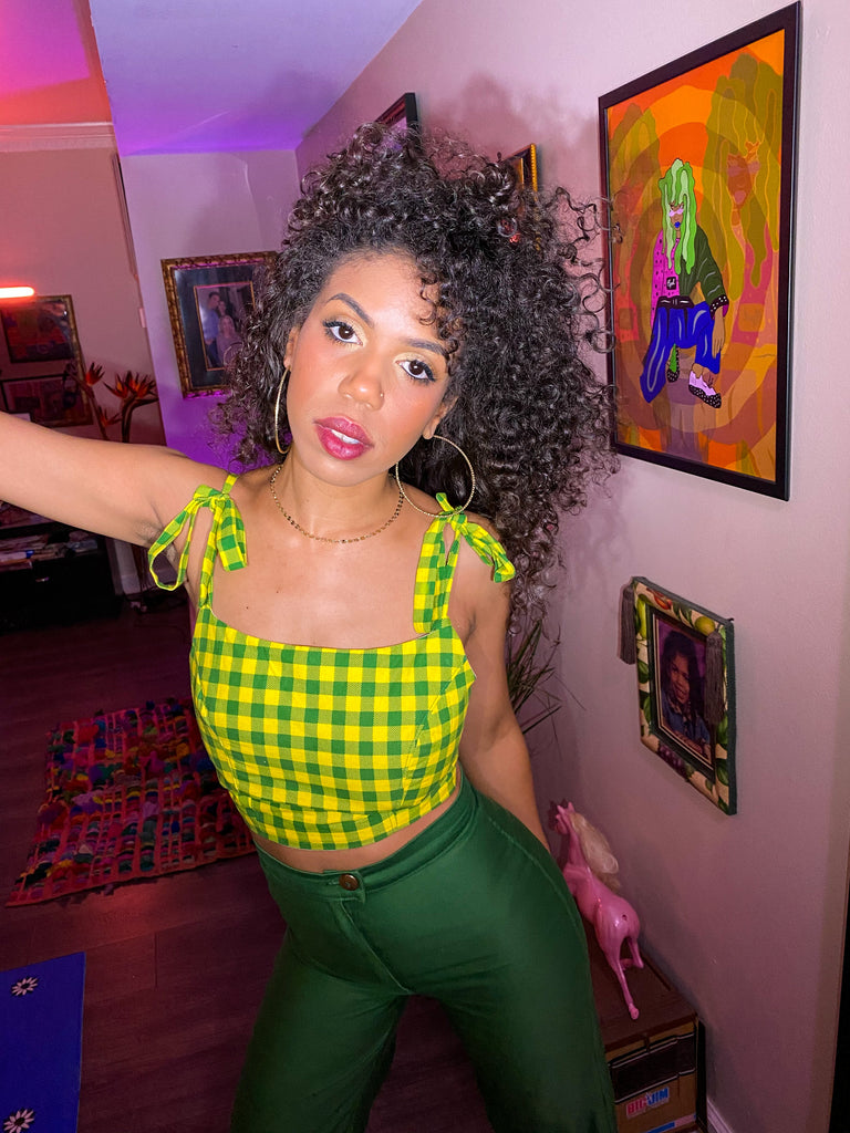 Opal Dillard in a custom designed outfit with artbyopal Art by Opal Dillard on the walls in the living room. Beautiful Black woman in a fashion scene with bright colors, opal is wearing a green and yellow checkered top and curly hair. Artbyopal art